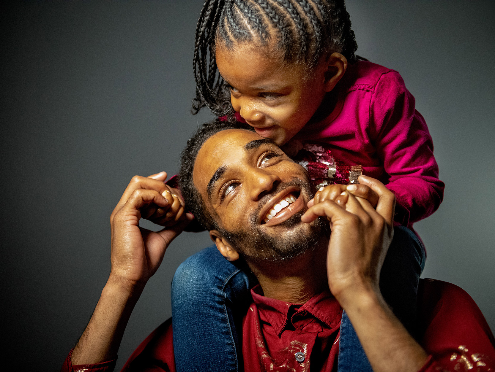 daughter sitting on her father's shoulders while he looks up at her smiling